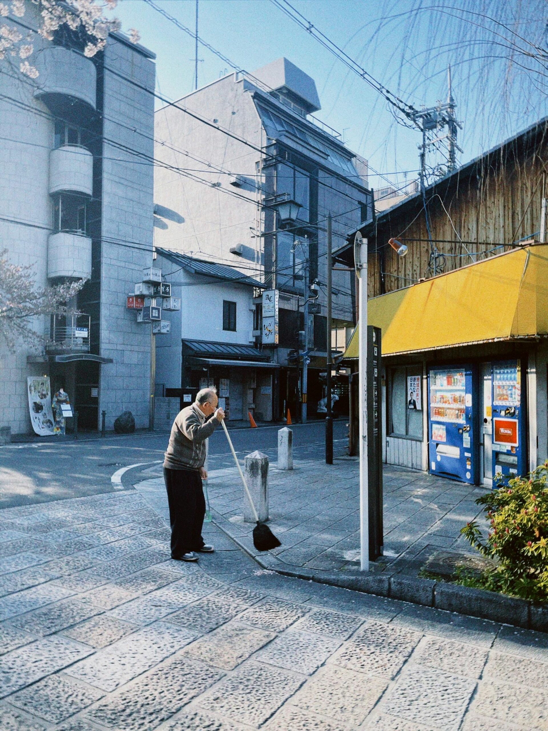 An elderly man cleaning a city street on a quiet day, urban life scene.
